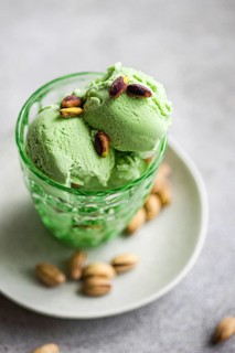 A scoop of creamy green pistachio ice cream with nuts is displayed in an ornate glass dish,