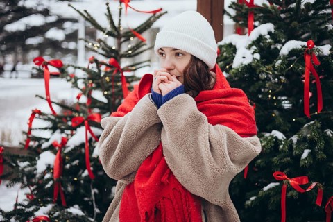 A young woman in a white beanie and red scarf stands cozily wrapped in a fluffy coat against a