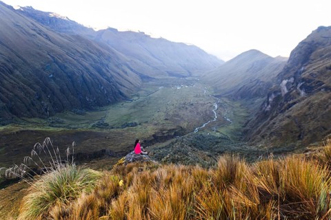 Ecuadorian woman in pink jacket peacefully gazes over the expansive, lush valley from El Altar