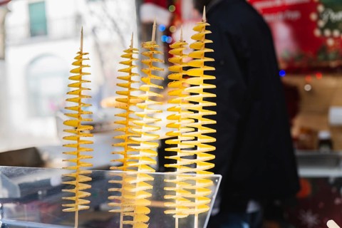 Close-up of spiral tornado potatoes on sticks displayed at an outdoor market. The vibrant yellow