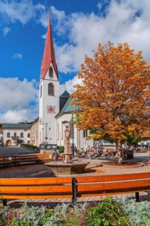 Fountain on the village square with the pilgrimage church of St. Oswald in autumn, Seefeld in