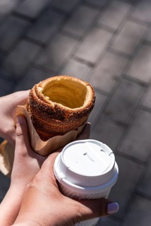 A boy holds a traditional trdelnik pastry in his hand, while a woman enjoys a cup of fresh coffee.