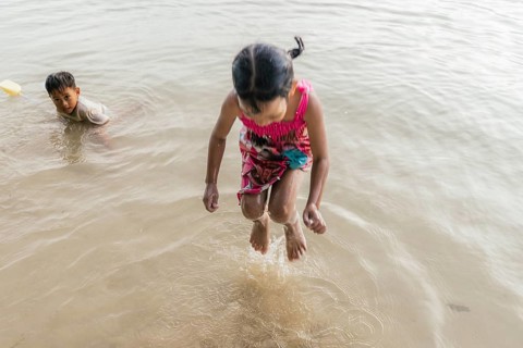 Children are playing joyfully at a beach in the Philippines. One child is jumping in shallow