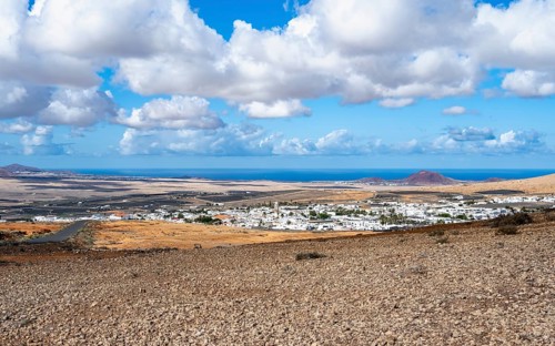 View of town, white houses of Teguise with church tower in dry volcanic landscape, view from