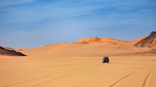 An off-road vehicle drives through a vast desert landscape with sand dunes, With off-road vehicles