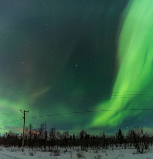 Brilliant green Aurora Borealis illuminates the night sky above a snowy landscape in Kiruna,