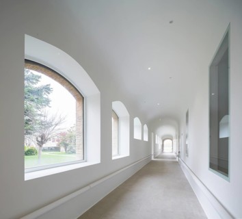 A luminous corridor of hospital featuring large arched windows, allowing ample natural light. The