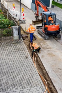 Construction workers lay fibre optic cable in trench under asphalt, cable trench, excavator,
