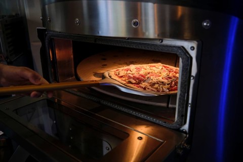 Cook using wooden peel to put pizza with ham and mushrooms into professional oven