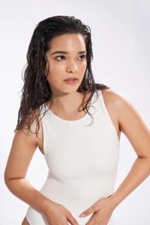 Studio portrait of a young woman dressed in a white bodysuit, featuring wet hair and delicate face