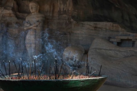 A serene scene of incense sticks burning with smoke rising in front of an ancient stone Buddha