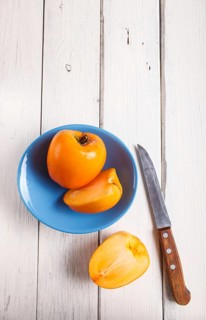 Ripe orange persimmon in a blue plate on white wooden background, with copy space