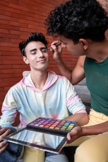 A joyful gay couple sharing a tender moment as one applies makeup to the other's face. They sit