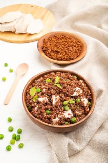 Quinoa porridge with green pea and chicken in wooden bowl on a white wooden background and linen