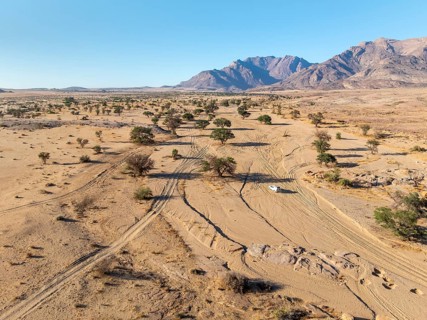 Aerial view of off-road car driving in dry riverbed and desert landscape on the Ugab River, behind
