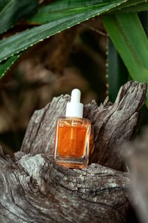 A bottle of golden Vitamin C serum for facial care sits perched on a gnarled tree trunk, surrounded