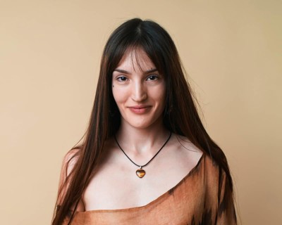 A portrait of a young woman posing gracefully against a beige background in a studio setting. She