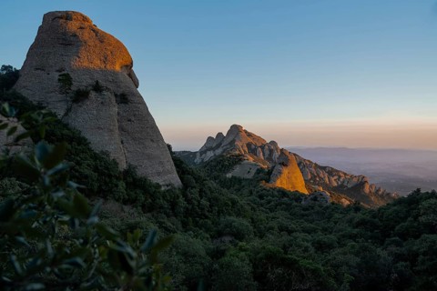 Dramatic rocky formations bathed in the warm glow of the setting sun, casting shadows over lush