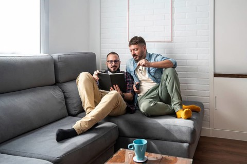 A gay couple sits comfortably on a sofa, enjoying a book together in a cozy living room setting,