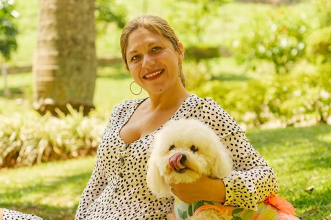 Happy woman embracing her cute white bichon frise dog while enjoying a sunny day in a park,