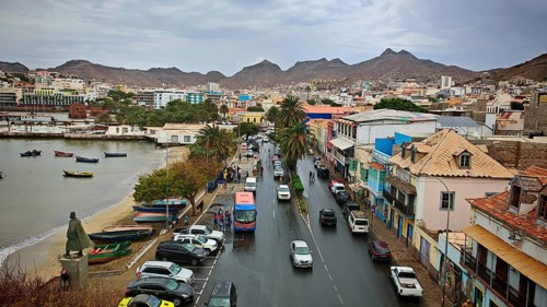 Busy city street along the coast with cars and palm trees, surrounded by mountains, view from Torre