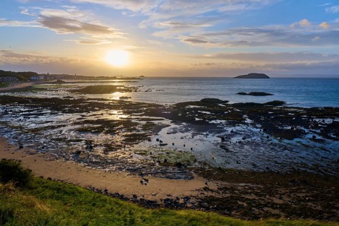 Beach landscape with sea and rocks at sunset under a cloudy sky, North Berwick, East Lothian,