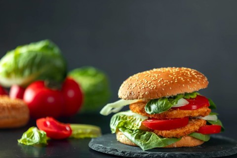 Burger with schnitzel, tomatoes, onions and lettuce, ingredients in the background