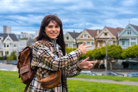 Young woman tourist visiting alamo square, pointing to the iconic victorian houses with a cityscape