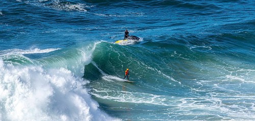 Surfers with their jet ski pilots in the Atlantic waves below Farol de Nazaré, Forte São Miguel,