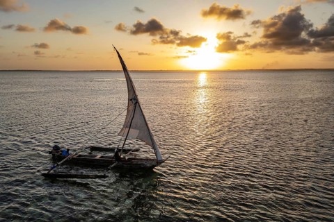 Traditional sailboat against a serene, golden sunset on calm water