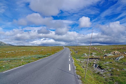 Asphalt road under wide blue sky with clouds nestled in peaceful countryside, Fell, Valdresflyra,