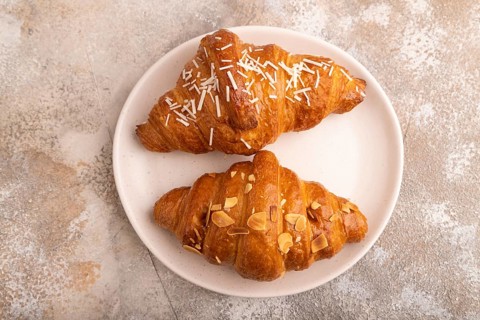 Croissant on white plate on brown concrete background, top view, flat lay, close up