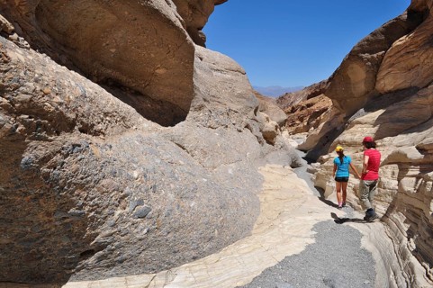 Two people hiking through a sunny gorge with large rock formations, Death Valley National Park,