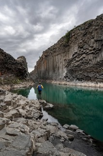 Tourist standing by the river in Stuðlagil Canyon, turquoise blue river between basalt columns,