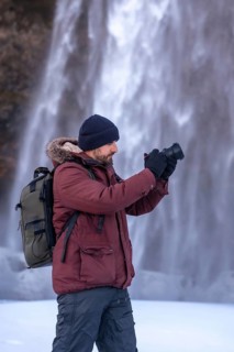 A photographer taking pictures in winter at the Seljalandsfoss waterfall with snow in Iceland