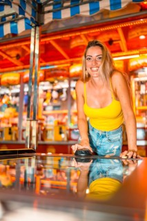 Vertical photo of a happy woman playing air hockey and having fun in an amusement arcade