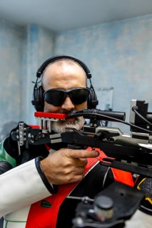 Blind athlete wearing headphones and specialized gear aims a rifle during an Olympic shooting