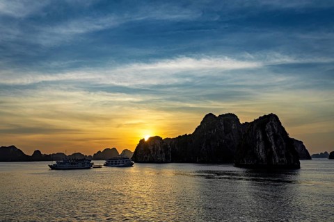 Boats sail past jagged rocks on a calm sea at sunset, sunset in Halong Bay in Vietnam