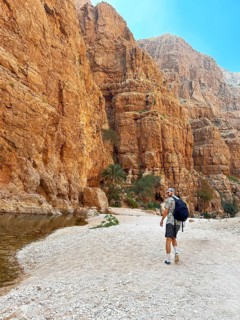 A male hiker walks along the rocky terrain of Wadi Ash Shab, a picturesque oasis nestled in Oman,