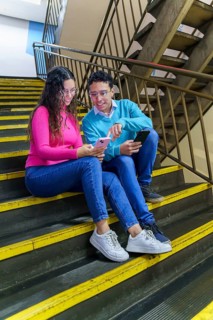 A young woman and a young man, both Gen Z, sit on a staircase sharing a moment with their
