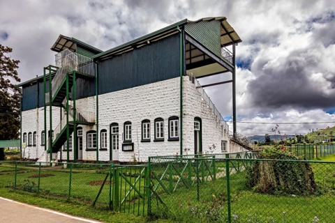 Historic building with outdoor stairs and sports stand surrounded by green areas and cloudy skies,