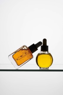 Two pipette bottles filled with vitamin C serum rest on a glass shelf One bottle leans against the