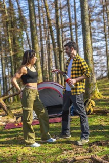 Hikers enjoying hot beverages at their campsite in a lush forest, sharing a moment of relaxation