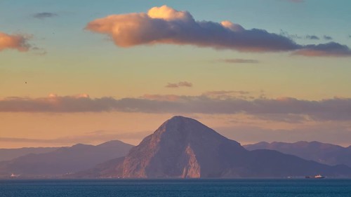 A majestic mountain rises from the sea under cloudy sky, New ferry port in southern Patras,