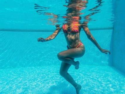 A woman in a colorful bikini is gracefully floating in a clear blue pool. Sunlight dances on the