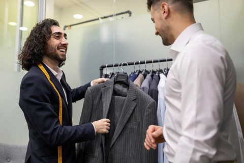 A tailor helps a customer choose a suit in a suit store. The tailor, with a measuring tape, offers