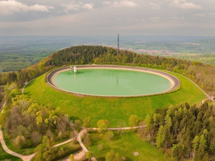 Reservoir on a hill surrounded by forest and meadows with observation tower in the background,