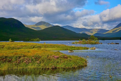 A peaceful lake surrounded by mountains, under a partly cloudy and blue sky, Rannoch Moor, Bridge