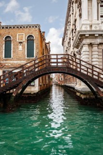 A picturesque Venice canal framed by historic buildings and a charming wooden bridge. The tranquil