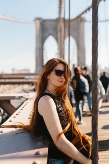 Young woman with long hair and sunglasses relaxing on a bridge during a sunny day in New York.
